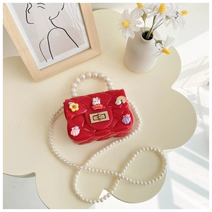 Detail view of red quilted silicone mini bag with pearl handle and cartoon charms