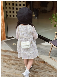 Detail shot of a small white quilted chain strap bag paired with a girl floral dress