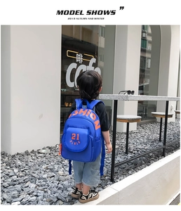 Toddler wearing a bright blue canvas backpack with orange lettering in an outdoor setting