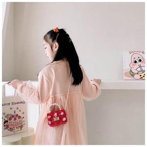 Detail of red quilted child's rabbit bag with elegant pearl strap on a young model