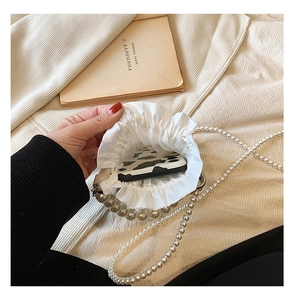 White pleated crossbody bag with pearl strap showing interior space for a smartphone