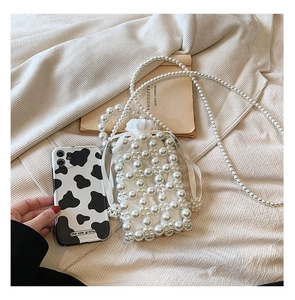 Detail view of woven faux pearl crossbody bag with beaded strap and cow print phone case
