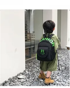 Detail of child wearing a black canvas backpack with green fashion lettering and padded straps