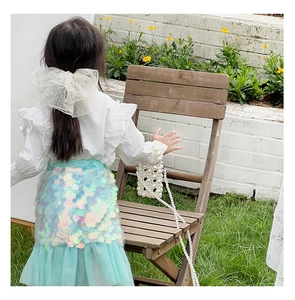 Rear view of girl in mint sequin skirt and white ruffle top with pearl woven bag