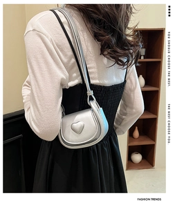 Silver mini heart-shaped crossbody bag shown on model with metallic finish and long strap