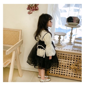Detail of elegant white puff sleeve top and black tiered mesh skirt with pearl bag