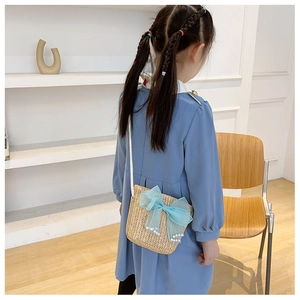 Close-up of a straw woven bag for girls featuring a blue mesh bow and pearl details