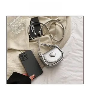 Size comparison of silver heart-shaped mini crossbody bag with a smartphone on white fabric