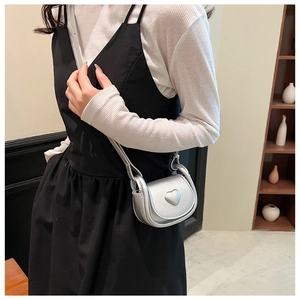 Mini silver saddle bag with heart relief detail worn by model over a black dress