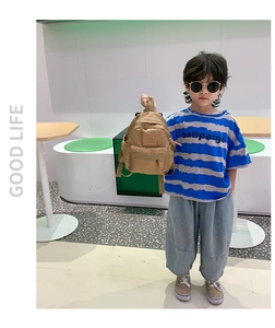 Toddler held a khaki mini backpack by the handle in a modern minimalist indoor setting