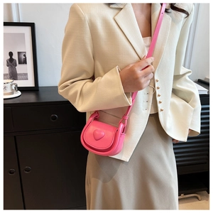Detailed close-up of a pink heart-embossed mini crossbody bag worn with a white blazer