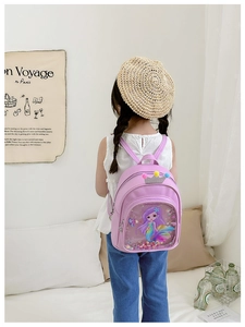 Pink mermaid toddler backpack with crown detail worn by child in a cozy room