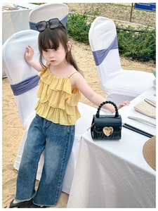 Detail eines gelben Rüschentops für Mädchen mit weiter Jeans und Herz-Handtasche