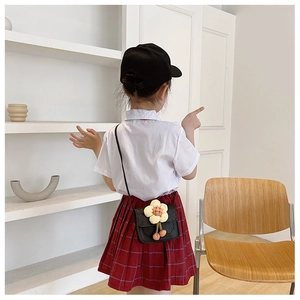 Detailed view of child wearing black PU crossbody bag with yellow sun flower and red charm