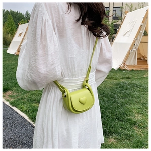 Outdoor shot of a lime green mini crossbody heart bag worn by a model on a lawn