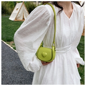 Mini sac à main vert avec cœur porté par une fille près d'une tente blanche