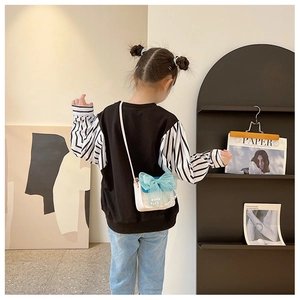 Rear view of a child wearing a beige PU leather crossbody bag with blue mesh bow detail