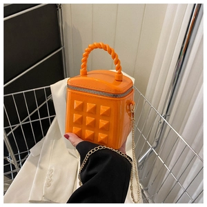 Close-up of bright orange mini box bag with 3D pyramid studs and golden chain strap