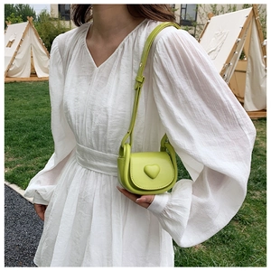 Détail du sac de selle vert citron à cœur sur robe blanche dans un jardin