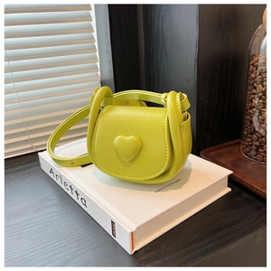 Detail of lime green mini saddle bag with heart decoration on a decorative book