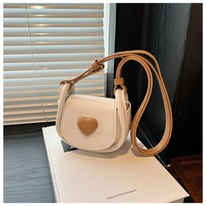 Detailed macro view of a cream mini saddle bag featuring a brown 3D heart on the flap