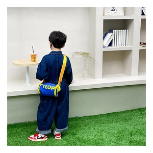 Détail du sac cylindre bleu pour enfants avec sangle jaune sur un garçon en denim