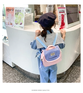 Zaino rosa per bambini con patta a quadretti blu, indossato da un bambino all'aperto