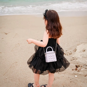 Girl in black dress holding a purple quilted mini bucket bag on a scenic beach