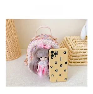 Detailed view of pink tweed girls backpack with pearl trim and doll accessory next to phone