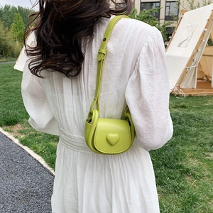 Sac à bandoulière vert fruit en forme de cœur porté par un mannequin en extérieur