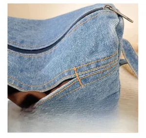 Detailed close-up of light blue denim fabric bag with neat brown stitching and metal zipper