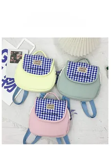 Vista piatta di zaini in tela per bambini con patte a scacchi blu in giallo rosa e verde