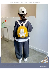 Detail view of a yellow canvas toddler backpack with a white plush bunny doll accessory