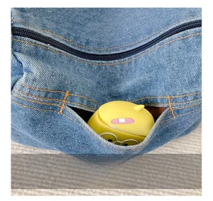Detail of denim shoulder bag featuring a smooth zipper pocket and contrast yellow stitching