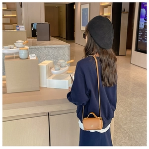 Girl wearing a minimalist brown leather mini crossbody bag in a stylish cafe setting