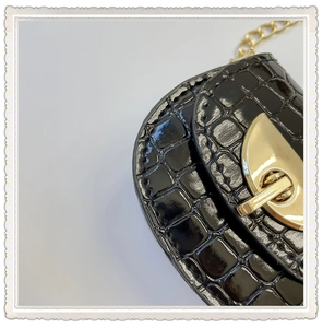 Detail of glossy black crocodile embossed saddle bag with gold metal buckle and chain