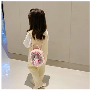 Detail of pink sequin girl's backpack featuring a doll ornament and pearl trim on a model