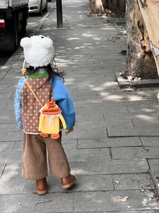 Detail of a handmade orange crochet duck crossbody bag paired with a knit cardigan and bear hat