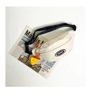 Détail du sac de poitrine en toile crème avec patch sport et breloque fromage jaune