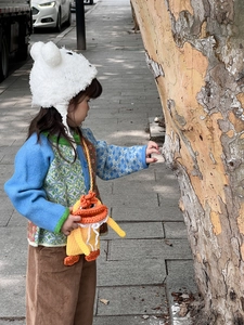 Outdoor shot of a kids' yellow knitted duck crossbody bag styled with a colorful cardigan