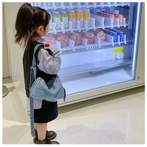 Detail view of a child wearing the light blue denim crossbody bag at a vending machine