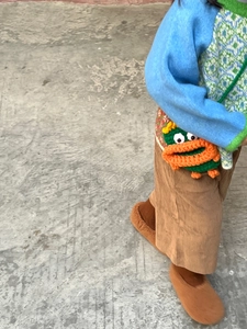 Détail d'un enfant portant un sac bandoulière monstre en tricot vert avec détails crochet