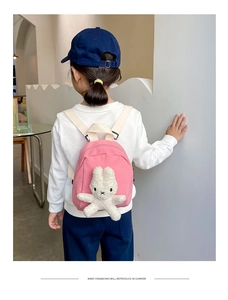 Rear view of a child wearing a pink canvas backpack with a white plush bunny detail