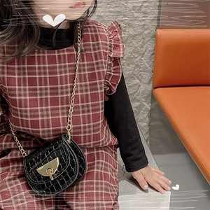 Detail of a black crocodile pattern mini saddle bag with golden chain and metal buckle