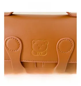 Detail showing bear logo and rivet buckle on brown PU leather backpack for kids