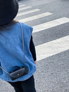 Gros plan d'un mini sac bandoulière en cuir noir avec bouton pression doré pour enfants