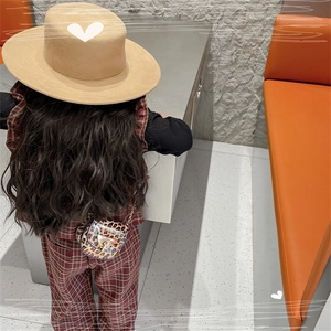 Rear view of child wearing leopard print chain saddle bag with red plaid overalls and hat