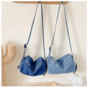 Detail view of denim crossbody bags in dark and light blue hanging on a wooden rack