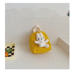 Detail of yellow canvas kids backpack featuring a plush white bunny and woven handle
