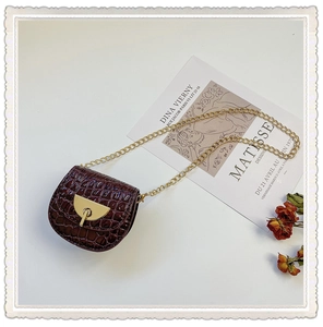 Detail of burgundy crocodile pattern mini saddle bag with golden chain strap and clasp